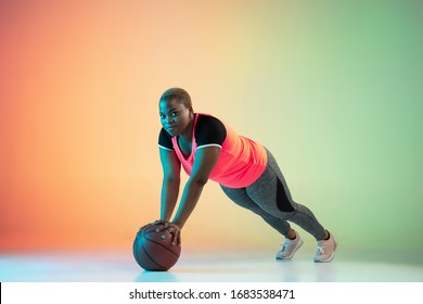 Young African-american Plus Size Female Model's Training On Gradient Background In Neon Light. Doing Workout Exercises With Fit Ball. Concept Of Sport, Healthy Lifestyle, Body Positive, Equality.