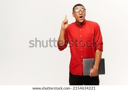Young African-American short-cutted student in glasses holds laptop and finger point up isolated on white background, guy in red shirt excited with breakthrough. Tech geek come with task solution
