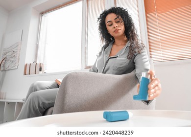 Young African-American woman with book taking asthma inhaler from table at home - Powered by Shutterstock