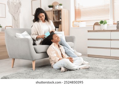 Young African-American woman brushing hair her daughter at home - Powered by Shutterstock