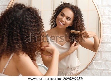 Young African-American woman combing her hair near mirror in bathroom