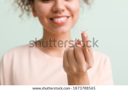 Young African-American woman with contact lens on color background