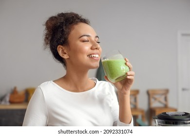 Young African-American woman drinking fresh smoothie in kitchen - Powered by Shutterstock