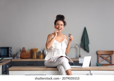 Young African-American woman eating chocolate in kitchen - Shutterstock ID 2079035515