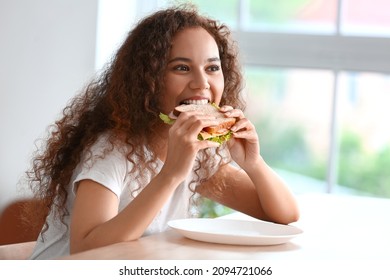 Young African-American woman eating tasty sandwich in kitchen - Powered by Shutterstock