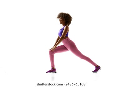 Young African-American woman in fashion activewear doing lunges in motion against white studio background. Concept of sport, mourning routine, active and healthy lifestyle, energy, action.
