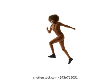 Young African-American woman in fashion brown activewear running in motion against white studio background. Concept of sport, mourning routine, active and healthy lifestyle, energy, action.