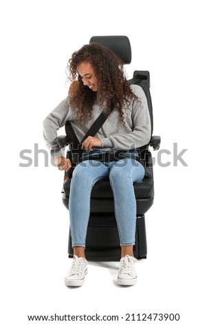 Young African-American woman fastening in car seat on white background