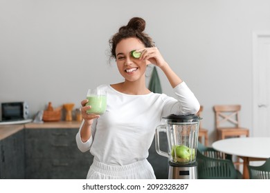 Young African-American woman with fresh smoothie and cucumber slice in kitchen - Powered by Shutterstock