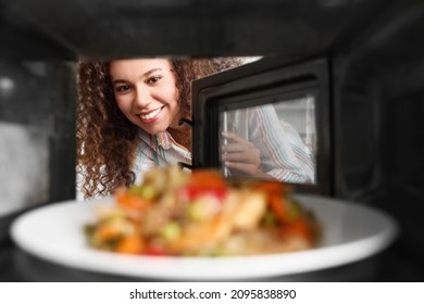 Joven afroamericana calentando comida en horno microondas, vista desde adentro