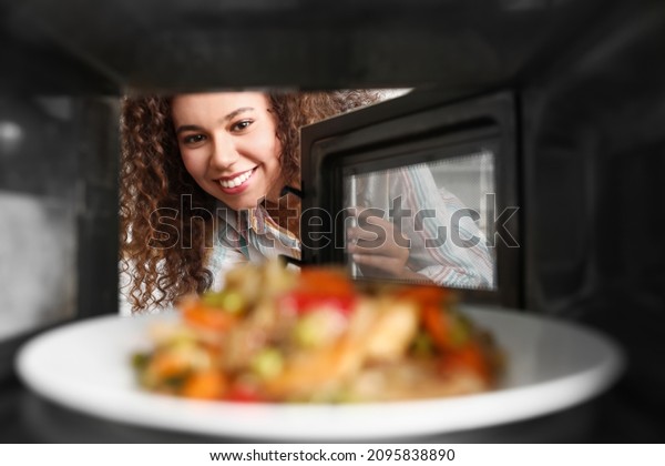 Young African-American woman heating food in\
microwave oven, view from\
inside