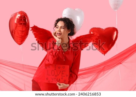 Young African-American woman holding paper with text I LOVE YOU on pink background. Valentine's Day celebration