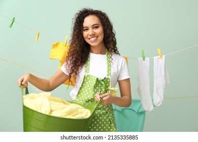 Young African-American woman with laundry basket and clothespins on color background