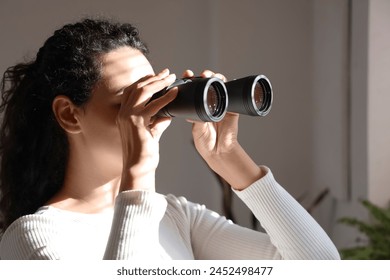 Young African-American woman looking through binoculars in window at home, closeup - Powered by Shutterstock