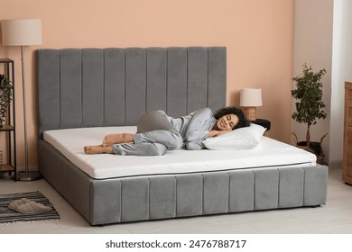 Young African-American woman with pillow lying on soft mattress in bedroom