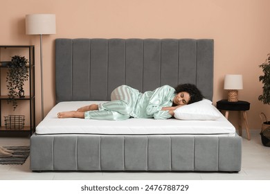 Young African-American woman with pillow lying on soft mattress in bedroom