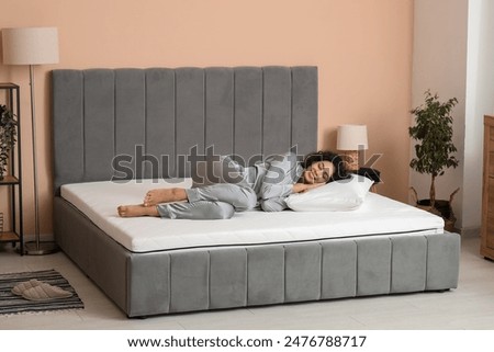 Young African-American woman with pillow lying on soft mattress in bedroom
