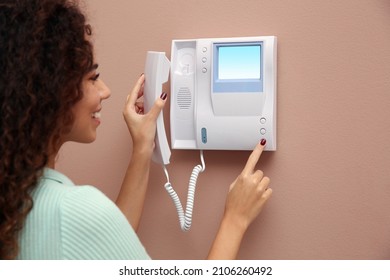 Young African-American woman pressing button on intercom panel indoors