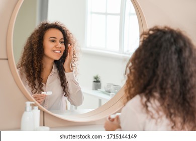 Young African-American woman putting in contact lenses at home