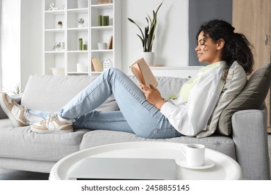 Young African-American woman reading book on sofa at home - Powered by Shutterstock