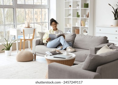 Young African-American woman reading magazine on sofa at home - Powered by Shutterstock