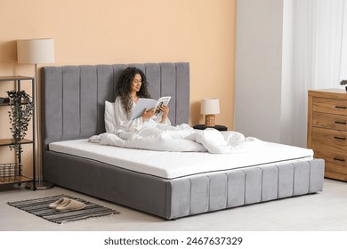 Young African-American woman reading magazine on soft mattress at home