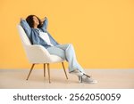 Young African-American woman resting in white armchair near orange wall