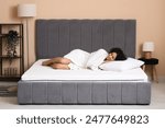 Young African-American woman in robe with pillow lying on soft mattress at home