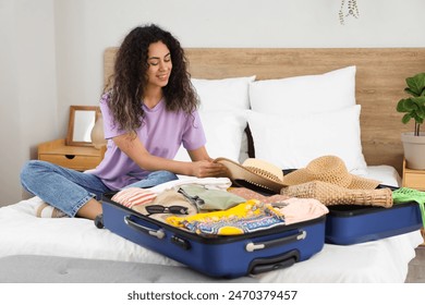 Young African-American woman unpacking suitcase with clothes in hotel room - Powered by Shutterstock