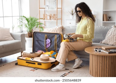 Young African-American woman unpacking suitcase with travelling accessories on sofa in hotel room - Powered by Shutterstock