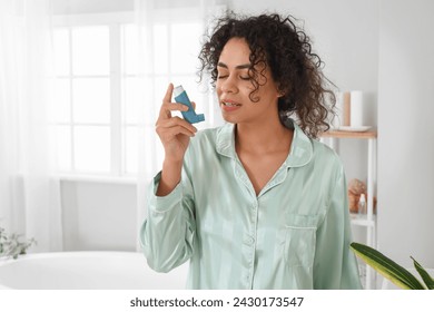 Young African-American woman using asthma inhaler in bathroom - Powered by Shutterstock