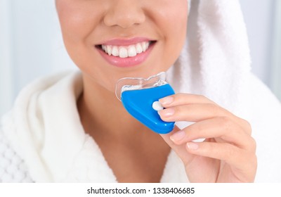 Young African-American Woman Using Teeth Whitening Device On Light Background, Closeup