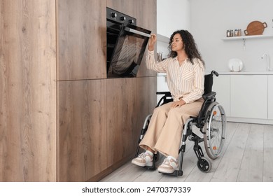 Young African-American woman in wheelchair opening oven at home - Powered by Shutterstock