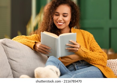 Young African-American woman in yellow cardigan reading book on sofa at home - Powered by Shutterstock