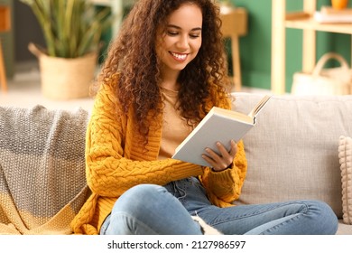 Young African-American woman in yellow cardigan reading book on sofa at home - Powered by Shutterstock