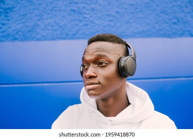 Young afro American black man listening music with wireless headphones while wearing a white sweatshirt, looking to the side
