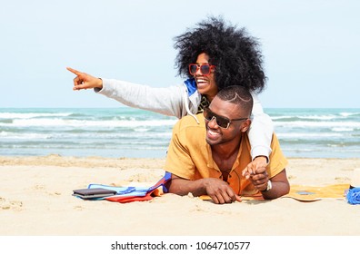 Young afro american couple  pointing finger relaxing on beach - Cheerful african friends having fun at day on blue ocean background - Concept of lovers happy moments on summer holiday - Vintage filter