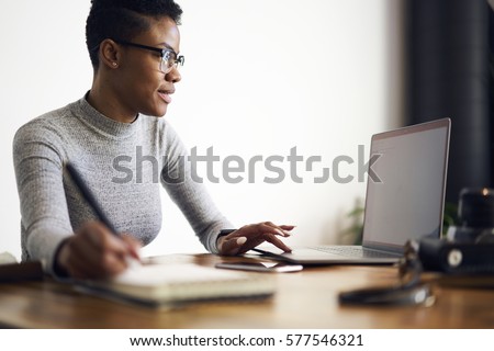 Young afro american female executive  filling in application on official site of media marketing corporation ordering services and collaboration via laptop computer and wireless internet indoor