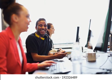 Young Afro American Man Looking At Camera Smiling While Working On Computer In Modern Classroom. Young Students Sitting At College Computer Lab.