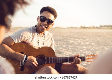 Young Afro American Man Playing Guitar For Friends While Sitting On The Beach