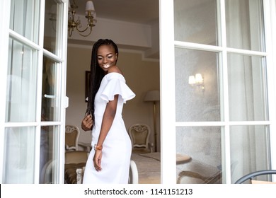 Young Afro American Woman With African Braids Or Dreadlocks. Girl Standing Near The Open Glass Door Or French Window.