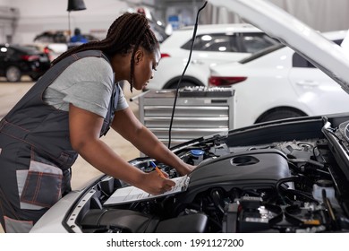 Young Afro American Woman Mechanic Holding Clipboard Checklist At Service Center Repair, Side View On Confident Serious Black Female At Work, Thinking. In Auto Service