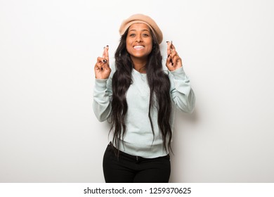 Young afro american woman on white wall with fingers crossing and wishing the best