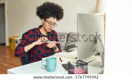 Young afro american woman using hand sanitizer, antiseptic gel while sitting at her workplace and working or studying online from home. Hygiene and Healthcare. Covid 19. Self isolation. Stay home