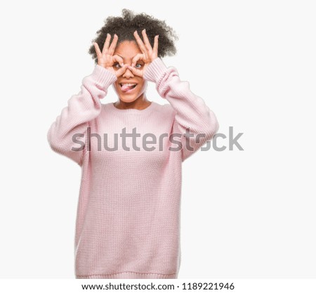 Young afro american woman wearing winter sweater over isolated background doing ok gesture like binoculars sticking tongue out, eyes looking through fingers. Crazy expression.