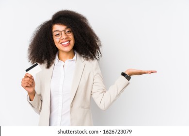 Young afro business woman holding a credit car isolated Young afro business woman holding a credit carshowing a copy space on a palm and holding another hand on waist.