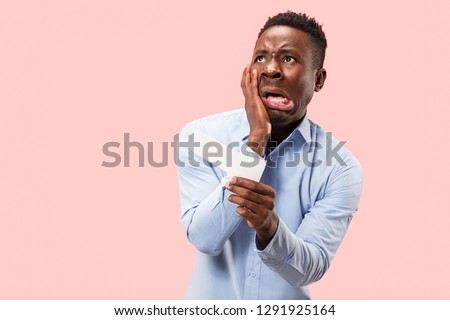 Young afro man with a surprised unhappy failure expression bet slip onpink studio background. Human facial emotions and betting concept. Trendy colors