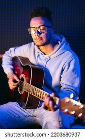 Young Afro Musician Wearing Glasses Playing Acoustic Guitar, On Dark Background