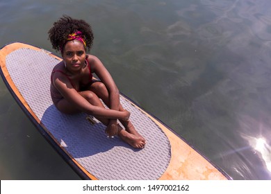 Young afro slim girl sitting on paddle Board in sea. - Powered by Shutterstock