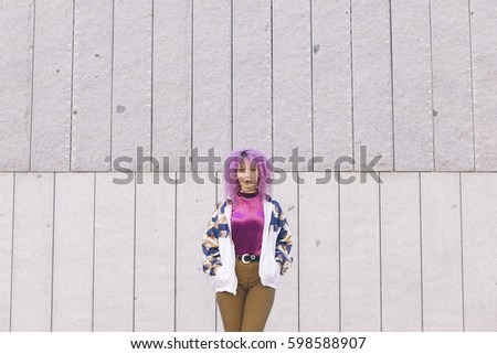 young afro woman standing against a wall wearing colorful clothes that match her purple hair
